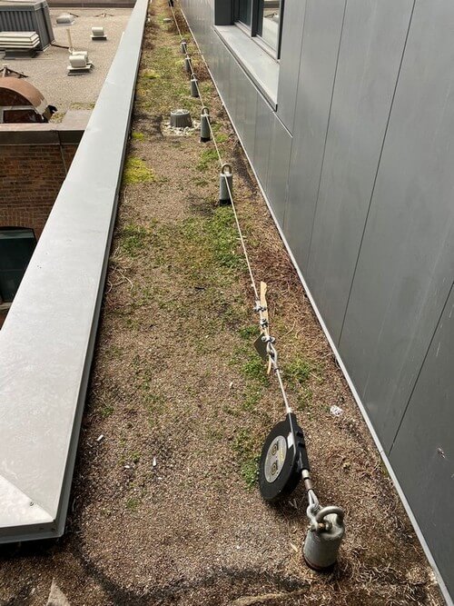 Aligned tieback anchors on a green patch of a roof with a horizontal lifeline running through them