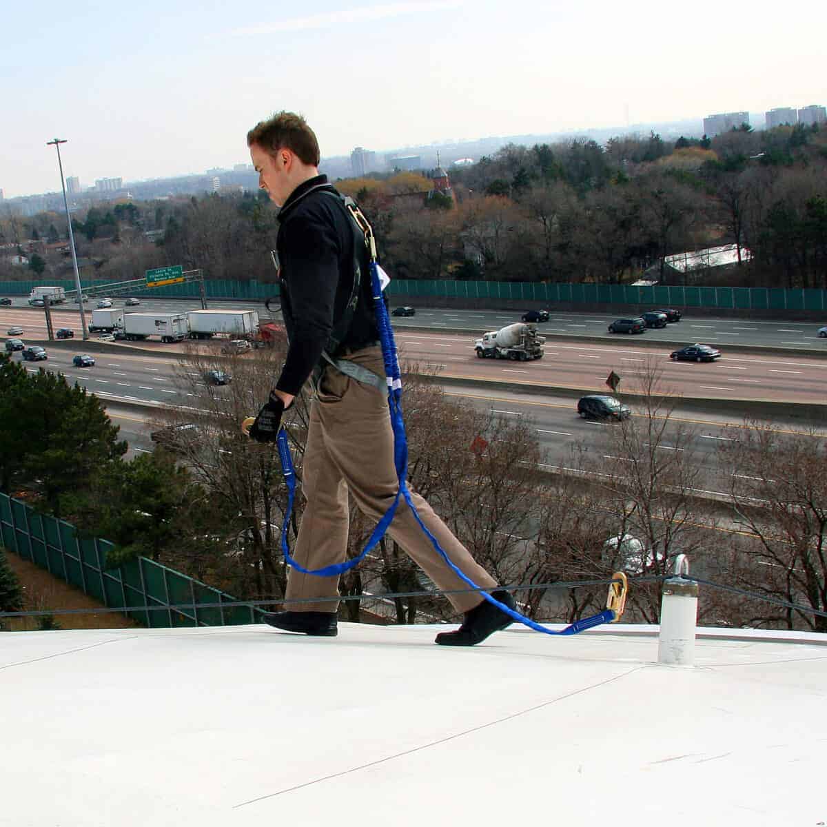 White man attached to horizontal lifeline as he walks along the roof edge