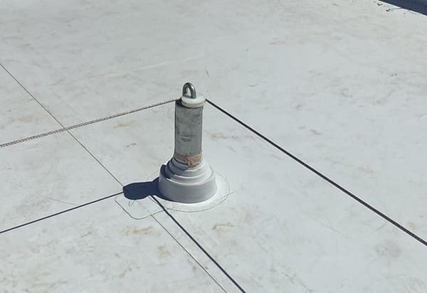 Corner tieback anchor of a standard horizontal lifeline system on a grey concrete roof