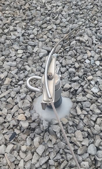 A tieback anchor for a hands free horizontal lifeline system on top of grey decorative stones