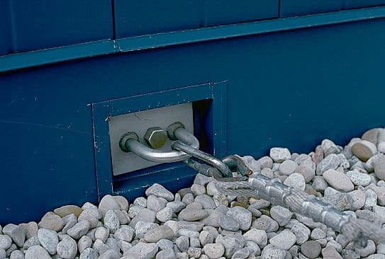 A residential blue wall with a U-bar tieback anchor installed in it, surrounded by decorative rocks