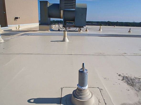 Several rooftop safety anchors on a concrete roof, aligned so a horizontal lifeline can pass through