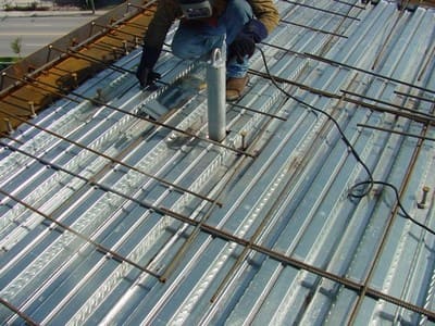 Welder next to newly installed tieback anchor on a steel panelled roof